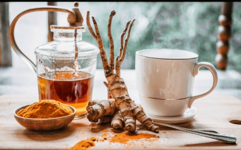 All Perfect Health: Turmeric root and powder next to a tea cup & kettle