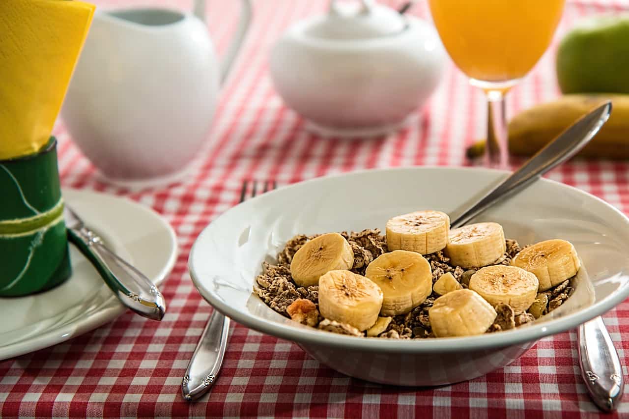 Bowl of bran cereal with slices of banana and glass of orange juice - allperfecthealth