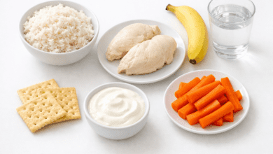 A clean, bright flat-lay photograph of bland diet foods arranged on a white surface: plain white rice, steamed chicken